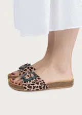 Sandalia plana con plantilla ergonómica y suela de corcho. Capellada de cuero con estampado animal print tipo leopardo y tira ancha ajustable con hebilla grande de resina translúcida en tono azulado.