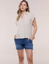 Camisa de lino de estructura recta, color beige con rayas verticales blancas. Cuenta con cuello solapa, escote en V abierto, abotonadura frontal, bolsillo plaqué en el pecho, mangas cortas de hombro caído y ruedo recto.