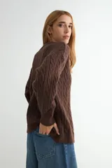 Cardigan de punto con diseño de trenzas, color beige, con escote en V, cierre frontal de botones negros y mangas largas con puños acanalados.