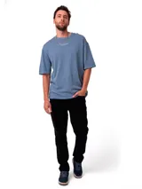 Remera de corte relajado color azul grisáceo, con cuello redondo y mangas cortas. Presenta un bordado sutil con el nombre de la marca en el pecho y un parche tejido en la manga.