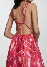 Vestido maxi de algodón con diseño estampado en tonos fucsia y naranja. Presenta escote en pico, tirantes finos dobles y espalda descubierta con cierre de lazo. Diseño evasé sin mangas.