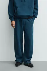 Pantalón jogger de corte relajado y pernera ancha, confeccionado en tejido de algodón con interior perchado. Presenta cintura elástica con cordón interior, bolsillos laterales y un bolsillo trasero de plastrón.