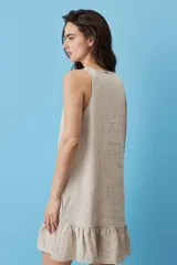 Vestido corto de lino color beige, de silueta suelta y sin mangas, con escote en V decorado con un botón, bolsillos laterales y detalle de volado en el ruedo.