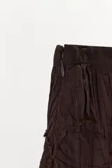 Pantalón de tiro bajo confeccionado en viscosa, con diseño abullonado y tejido plisado. Presenta detalles de apliques circulares en la cintura y terminaciones en los puños con tejido crochet a tono.