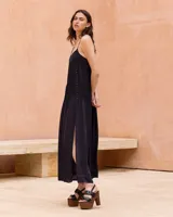 Vestido largo negro con tirantes finos ajustables, cuerpo con plisado fino y detalle de hilera de botones decorativos en el lateral. Cuenta con una falda amplia y fluida con abertura lateral.