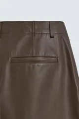 Pantalón de corte balloon fit confeccionado en piel, con bolsillos delanteros y traseros de vivo, cierre frontal con cremallera y botón.