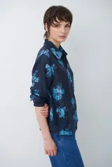 Camisa de corte clásico con cuello camisero y cierre frontal de botones, confeccionada en tela color bordó con estampado floral en tonos celestes.
