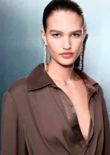 Camisa de tejido satinado color marrón, con cuello camisero cruzado, diseño recto y cierre de lazo cruzado en el lateral. Cuenta con mangas largas y puños anchos abotonados.
