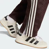 Pantalón deportivo Adidas color marrón, con diseño de monograma grabado en relieve en todo el tejido, franjas laterales blancas y el logo de la marca bordado en la cadera.