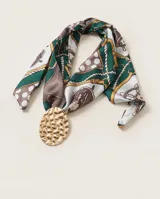 Pañuelo de seda estampado con diseño de cadenas, lunares y detalles geométricos en tonos verde, marrón, blanco y dorado. Incluye un dije ovalado dorado con textura martillada.