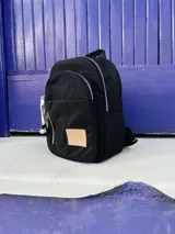 Mochila negra de nylon con cierre plateado y etiqueta con el logo de la marca en color beige.