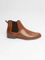 Botín tipo Chelsea de cuero sintético color marrón, con paneles elásticos laterales oscuros y suela de goma con pequeño tacón.