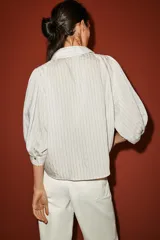 Camisa blanca a rayas sutiles, de cuello solapa y manga abullonada por debajo del codo. Presenta delicados bordados florales perforados en el frente y cierre frontal con botones.