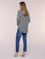 Camisa de corte clásico y silueta relajada con diseño de rayas verticales en blanco y negro. Presenta cuello camisero tradicional, cartera frontal con botones, un bolsillo aplicado en el pecho con rayas horizontales y mangas largas con sistema para arremangar.