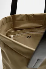 Bolso tipo shopper color beige, fabricado en tejido técnico con asas de mano de piel color negro. Tiene compartimento principal con cierre de imán y bolsillo interior con cremallera.