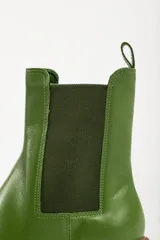Bota tipo chelsea con suela track de goma en color marrón y capellada de cuero negro. Presenta elásticos laterales y tirador trasero.