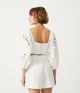 Blusa corta blanca de algodón con escote cuadrado, manga larga abullonada con bordados, y látex en la espalda.