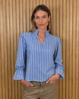 Blusa de algodón color azul, de corte suelto, con mangas largas abullonadas y cuello con volados y escote en V.