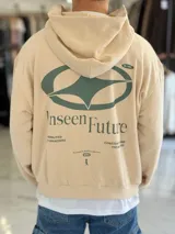 Hoodie de corte boxy fit color beige, con capucha y estampa gráfica verde en la espalda con la inscripción "Unseen Future" y detalles tipográficos.