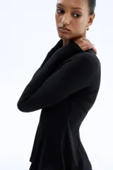 Top de manga larga confeccionado en punto de crepé, con cuello redondo y diseño de peplum. Presenta costuras moldeadoras en la parte frontal y posterior que definen la silueta.