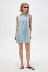 Vestido corto de jean blanco con tirantes anchos, cuello redondo, corte holgado y bolsillos laterales.
