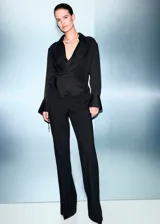 Camisa de tejido satinado color negro, de corte recto con diseño cruzado que se ajusta mediante un lazo lateral. Presenta cuello camisero, escote en V y mangas largas con puños anchos abotonados.
