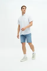Camisa de manga corta confeccionada en una mezcla de lino y algodón, con diseño de rayas verticales en tonos claros. Presenta cuello camisero con botones, cierre frontal abotonado y un bolsillo en el pecho con logo bordado.