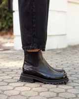 Botinetas tipo Chelsea de cuero negro, con paneles laterales elásticos y suela track dentada de goma. Presentan una combinación de texturas entre cuero mate y cuero charolado en la puntera y el talón.