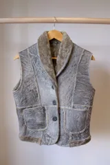 Chaleco de cuero genuino con interior de piel sintética, diseño con cuello solapa, cierre frontal de tres botones y dos bolsillos delanteros aplicados.