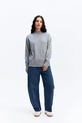 Sweater de tejido de punto color marrón con diseño estampado de flores en tonos rosados. Presenta cuello alto, mangas largas con puños ajustados y un corte relajado con terminación recta en la cintura.