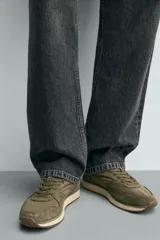 Zapatilla deportiva de estilo casual, confeccionada en una combinación de piezas de cuero con acabado de gamuza y paneles textiles. Presenta una horma redonda, cierre mediante cordones y una suela dentada en tono contrastante.
