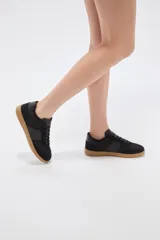 Zapatillas urbanas de color negro con suela de goma marrón, cordones negros con detalles blancos y paneles laterales.