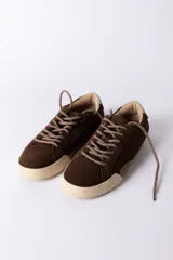 Championes urbanos de gamuza color marrón, con suela de goma en tono crema y cordones jaspeados. Presenta un refuerzo en la puntera y un detalle en cuero beige en el talón.