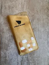 Portalentes rígido de cuero color beige, de la marca Carolina de Cunto, con diseño pintado a mano en tonos cobre, dorado y blanco, y el logo de la marca impreso en negro.