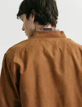 Campera tipo bomber de color marrón, confeccionada en tejido con textura similar a la gamuza, con cierre frontal completo, cuello redondo y puños elásticos.
