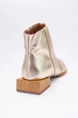 Botín de cuero dorado con punta fina y taco bajo cuadrado de madera.