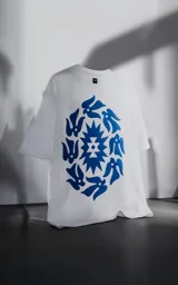 Remera blanca de corte holgado con estampa central en color azul que combina motivos geométricos tipo chakana con figuras de aves dispuestas en círculo.