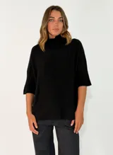 Sweater de punto color negro, con cuello alto y mangas cortas con puños acanalados. Presenta un diseño holgado y cómodo.