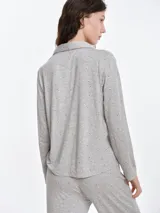 Camisa de pijama de manga larga con cuello solapa y cierre frontal de botones. Presenta un estampado sutil de pequeños corazones sobre una base de color gris melange, con detalles de ribete en contraste en el cuello y la botonera.