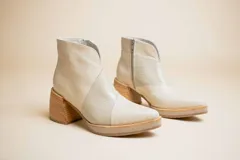 Botas cortas de cuero color crema, con puntera fina, paneles laterales con textura de piel de reptil, cierre lateral con cremallera y tacón geométrico de madera.