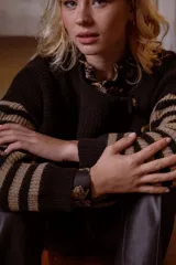 Sweater de punto en color crema con rayas horizontales en tono dorado. Presenta un diseño de cuello redondo con una solapa lateral decorada con botones metálicos dorados y corte holgado.