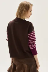 Sweater de cuello tortuga, tejido a rayas horizontales azul marino y blanco. Presenta un bordado de flor roja en el pecho y mangas largas con diseño de rayas en tonos de azul más claro.