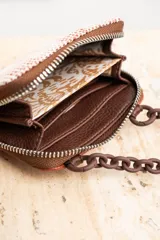 Cartera pequeña color terracota con textura tejida, cierre con cremallera y cadena gruesa marrón para colgar al hombro.