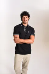 Polo de manga corta confeccionado en tejido interlock suave, color negro con detalles de vivos en color blanco en el cuello y las mangas. Presenta tapeta con botones y un bolsillo frontal con el logo bordado.