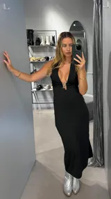 Vestido largo negro con escote halter y abertura en la pierna. Presenta un detalle metálico en el centro del escote.