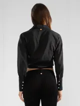 Camisa negra de manga larga con lazo en la cintura y botones nacarados. Confeccionada en 100% algodón y detalle de Polonio en cobre.