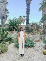 Top de tejido de punto color crema, con cuello alto y diseño sin mangas. Presenta un corte ajustado con laterales abiertos que se cierran mediante cordones ajustables.