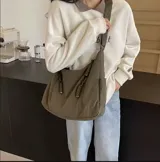 Cartera tipo hobo color verde oliva, de tela suave, liviana y espaciosa, con bolsillos frontales con cierre y correa ajustable al hombro.