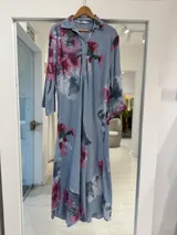 Vestido midi celeste con estampado floral en tonos fucsia y verde, cuello camisero, cierre frontal de botones y mangas largas.