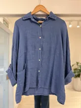 Camisa azul jean de lino con cierre frontal de botones, bolsillos aplicados y mangas largas con vuelta.